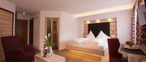 Una habitación de hotel moderna con una cama, un escritorio, dos sillas y una mesita de noche con un jarrón de flores.
