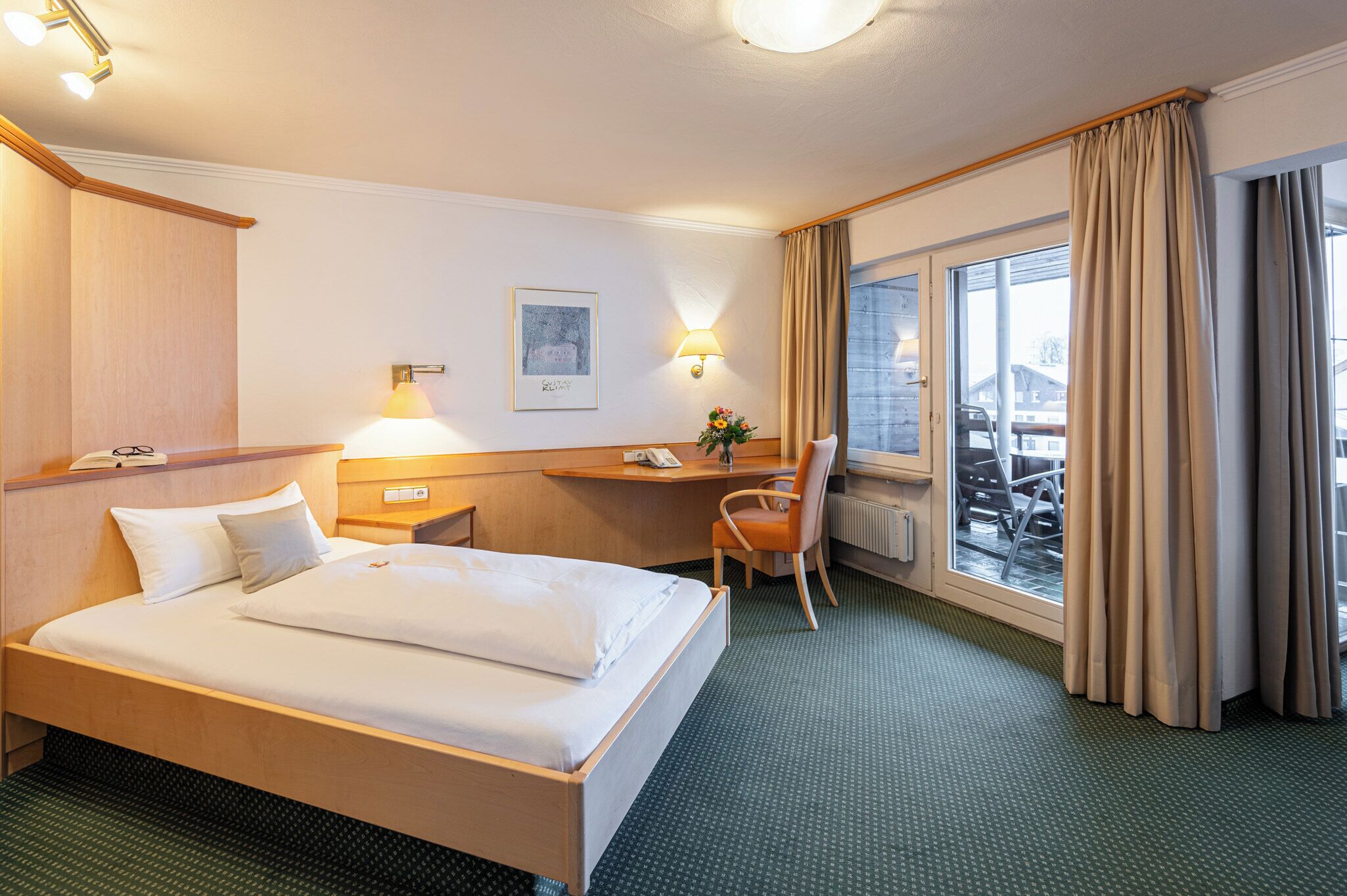 Una habitación de hotel con una cama grande, un escritorio con una silla, una lámpara y un ventanal con cortinas.