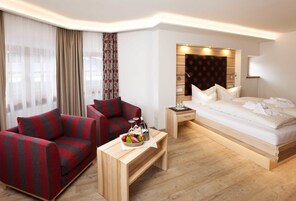 Una habitación de hotel moderna con un sofá, una mesita de noche con una cesta de fruta, una cama con ropa blanca y un cabecero de madera.