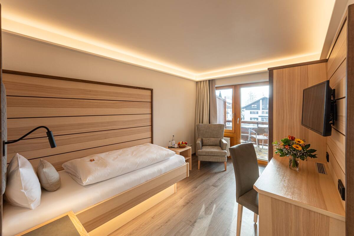 Une chambre d’hôtel moderne avec une tête de lit en bois, un lit, un bureau, une chaise et un téléviseur.