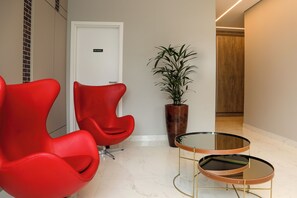 A modern waiting area with red chairs, a potted plant, and a glass table.