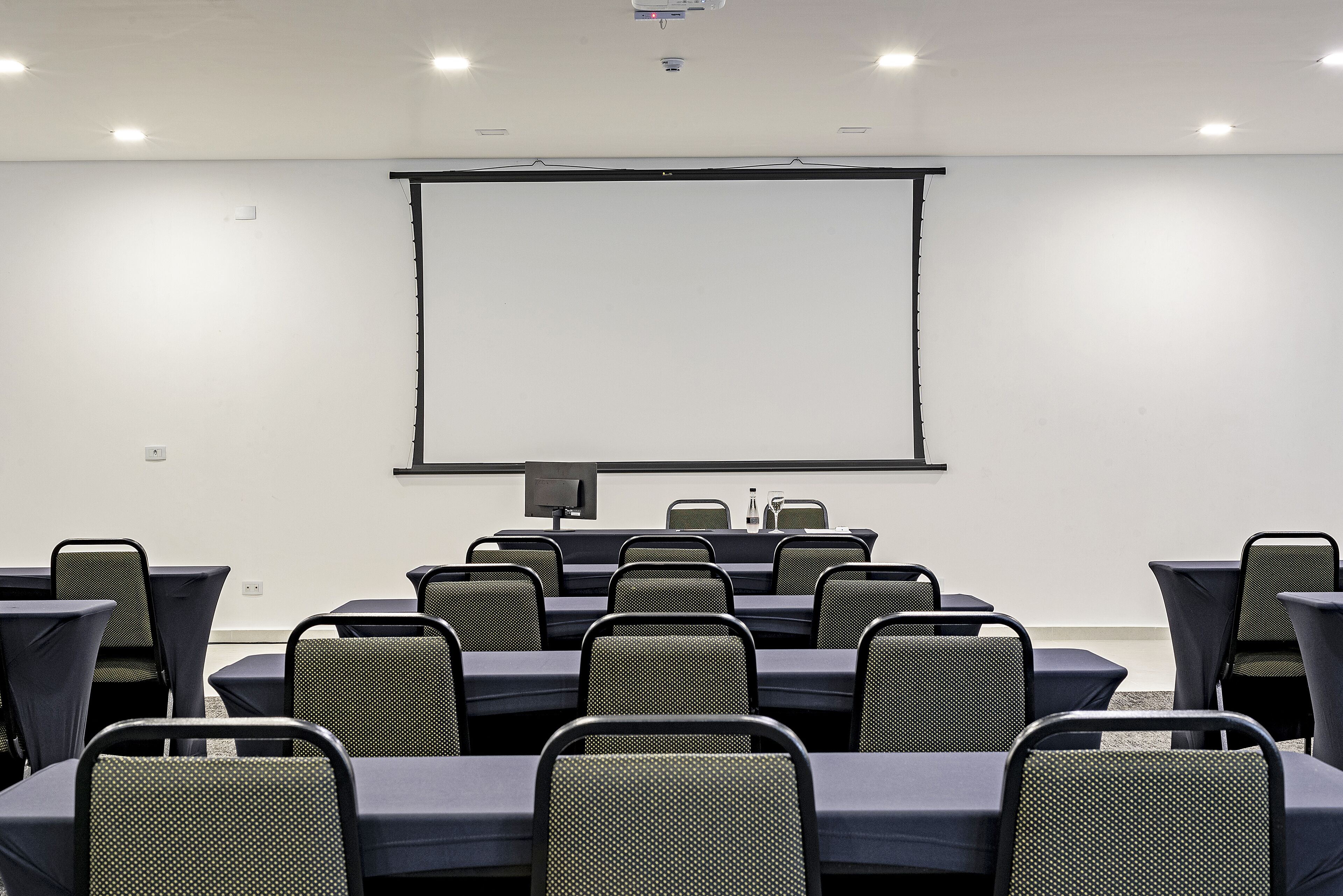 Una sala de conferències amb una gran pantalla de projecció, files de cadires i taules.