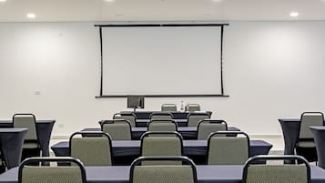Una sala de conferències amb una gran pantalla de projecció, files de cadires i taules.