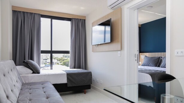 Ein modernes Hotelzimmer mit einem großen Bett, einer Couch, einem an der Wand montierten Fernseher und einem Balkon mit Vorhängen.