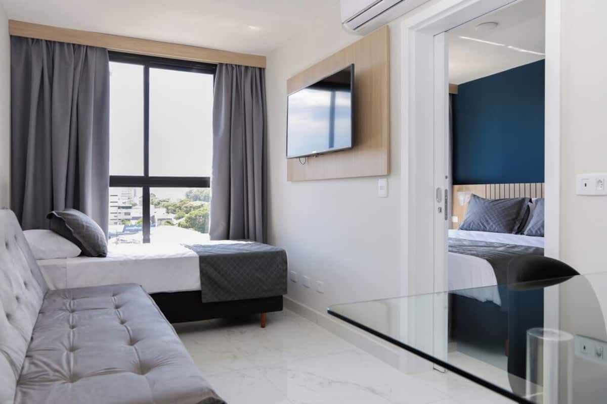 Ein modernes Hotelzimmer mit einem großen Bett, einer Couch, einem an der Wand montierten Fernseher und einem Balkon mit Vorhängen.