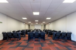 Une salle de conférence dotée de plusieurs tables et chaises, ainsi que de verres à eau et de microphones.
