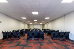 Un salón de conferencias con varias mesas y sillas, equipado con vasos de agua y micrófonos.