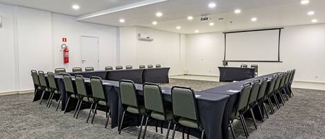 Un salón de conferencias con una larga mesa, sillas, una pantalla de proyector y un extintor.