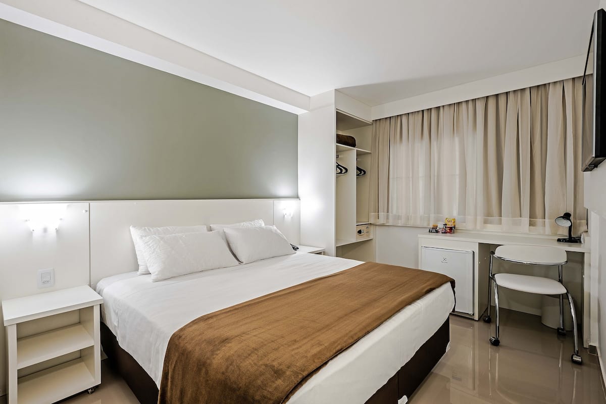 Ein Hotelzimmer mit einem Bett, Nachttischen, einem Schreibtisch mit Stuhl, einem Kleiderschrank und einem Fernseher.