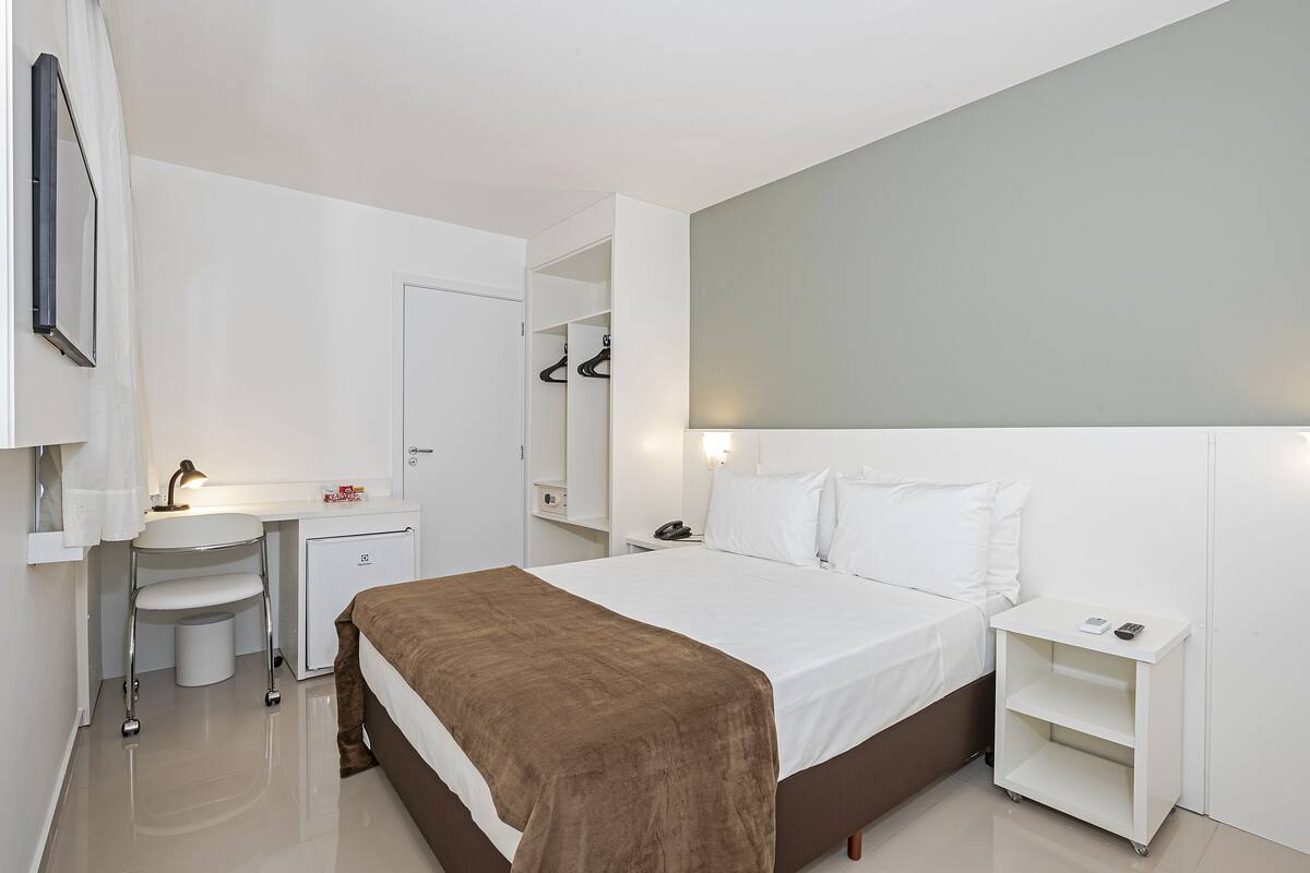 Ein modernes Hotelzimmer mit Bett, Schreibtisch, kleiner Kommode und Kleiderschrank.