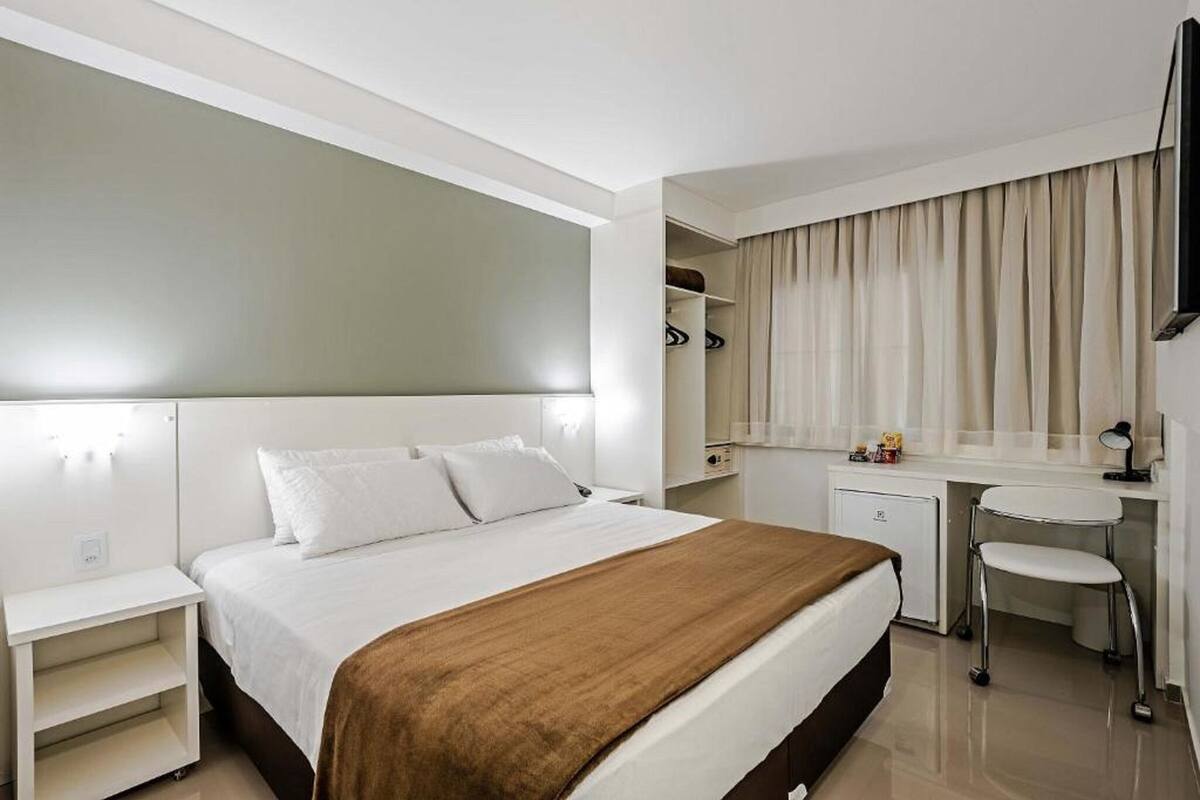 Ein Hotelzimmer mit Bett, Nachttisch, Schreibtisch, Stuhl und einer kleinen Küchenzeile.