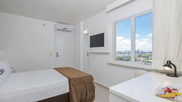 Quarto de hotel com cama, escrivaninha, televisão e janela com vista para a cidade.