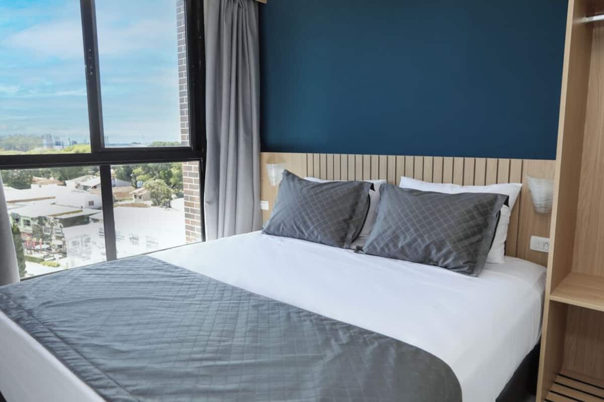 Ein Hotelzimmer mit einem großen Bett, Blick auf die Stadt durch ein Fenster und einem Holzkopfbrett.