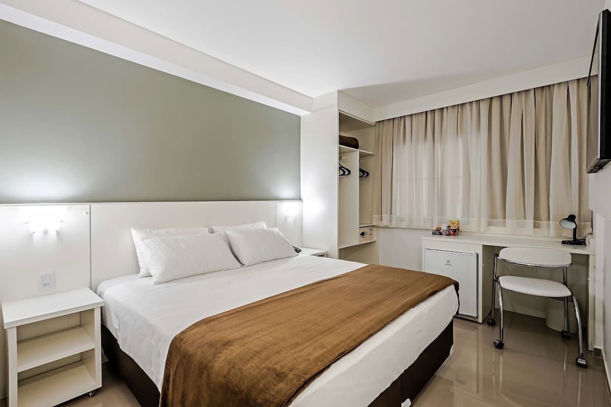 Ein Hotelzimmer mit Bett, Nachttischen, Schreibtisch, Stuhl, Spiegel und Kleiderschrank.
