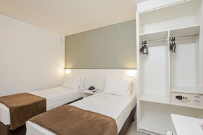 Una habitación de hotel con dos camas individuales, una mesita de noche con teléfono y lámpara, un armario con ropa colgada y un escritorio con silla.