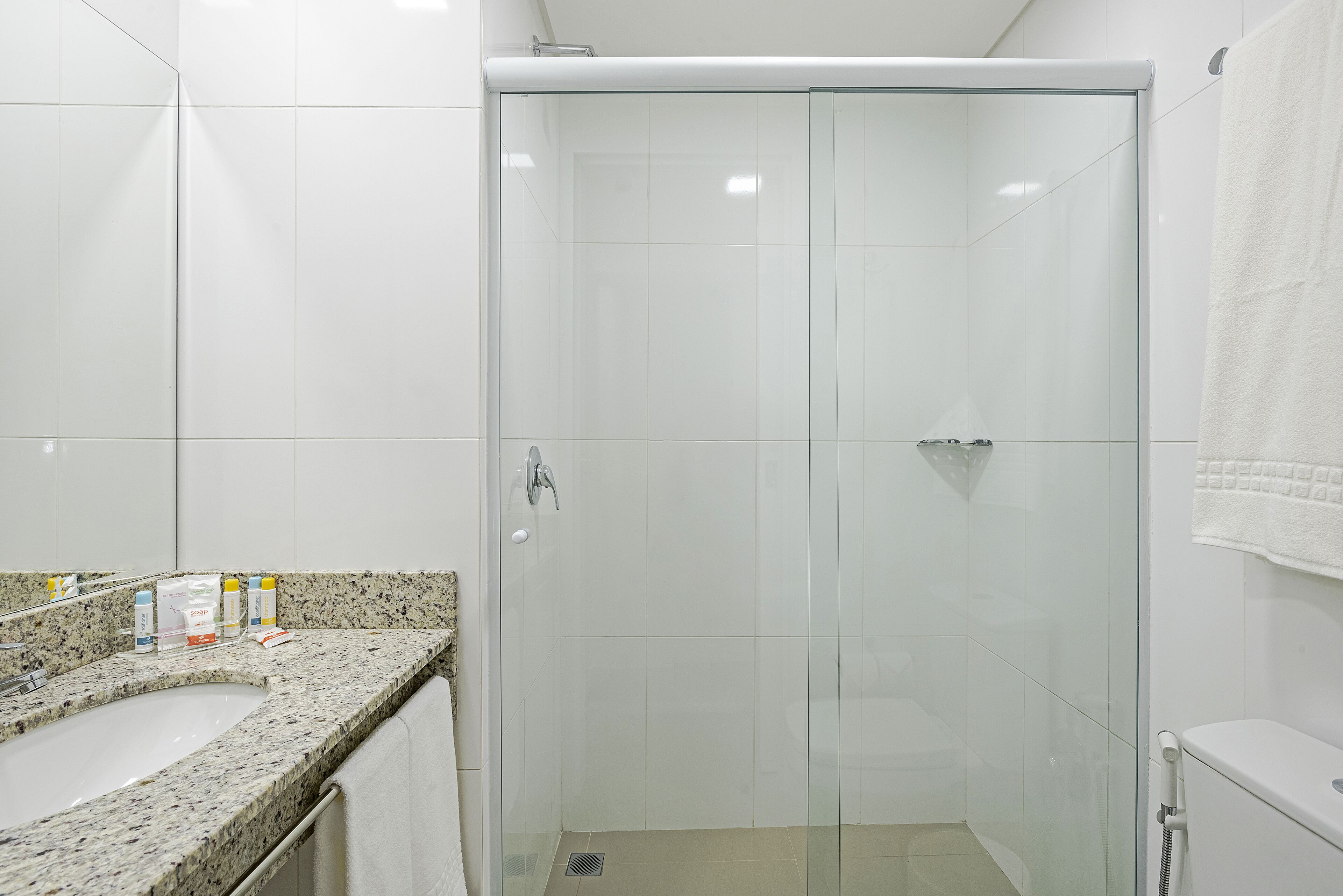 Un baño moderno con ducha envuelta en vidrio, encimera de granito y lavabo blanco.
