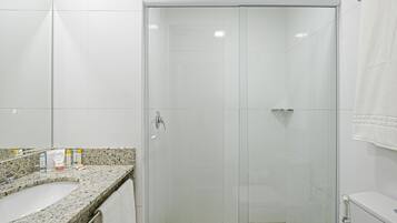 Un baño moderno con ducha envuelta en vidrio, encimera de granito y lavabo blanco.