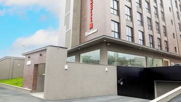 Edifício de hotel moderno com placa vermelha em destaque, entrada coberta e área de estacionamento.