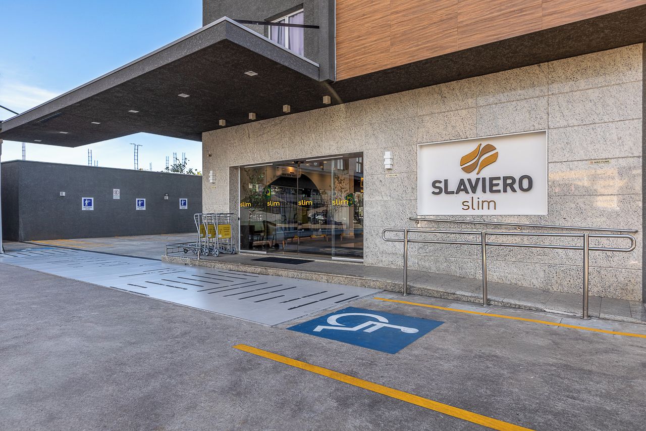 Entrada de un edificio con un letrero que dice 'Slaviere slim' y un espacio de estacionamiento accesible para sillas de ruedas.