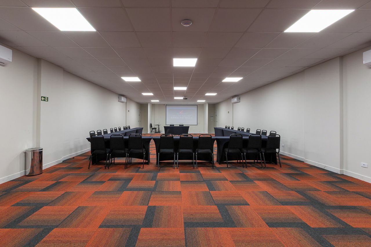 A conference room with a long table, chairs, a projector screen, and a carpeted floor.