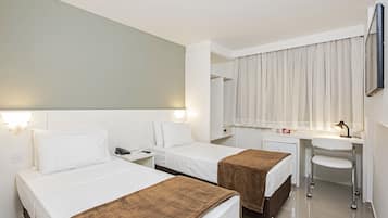Habitación de hotel con dos camas, un escritorio con silla, un refrigerador pequeño y un espejo.