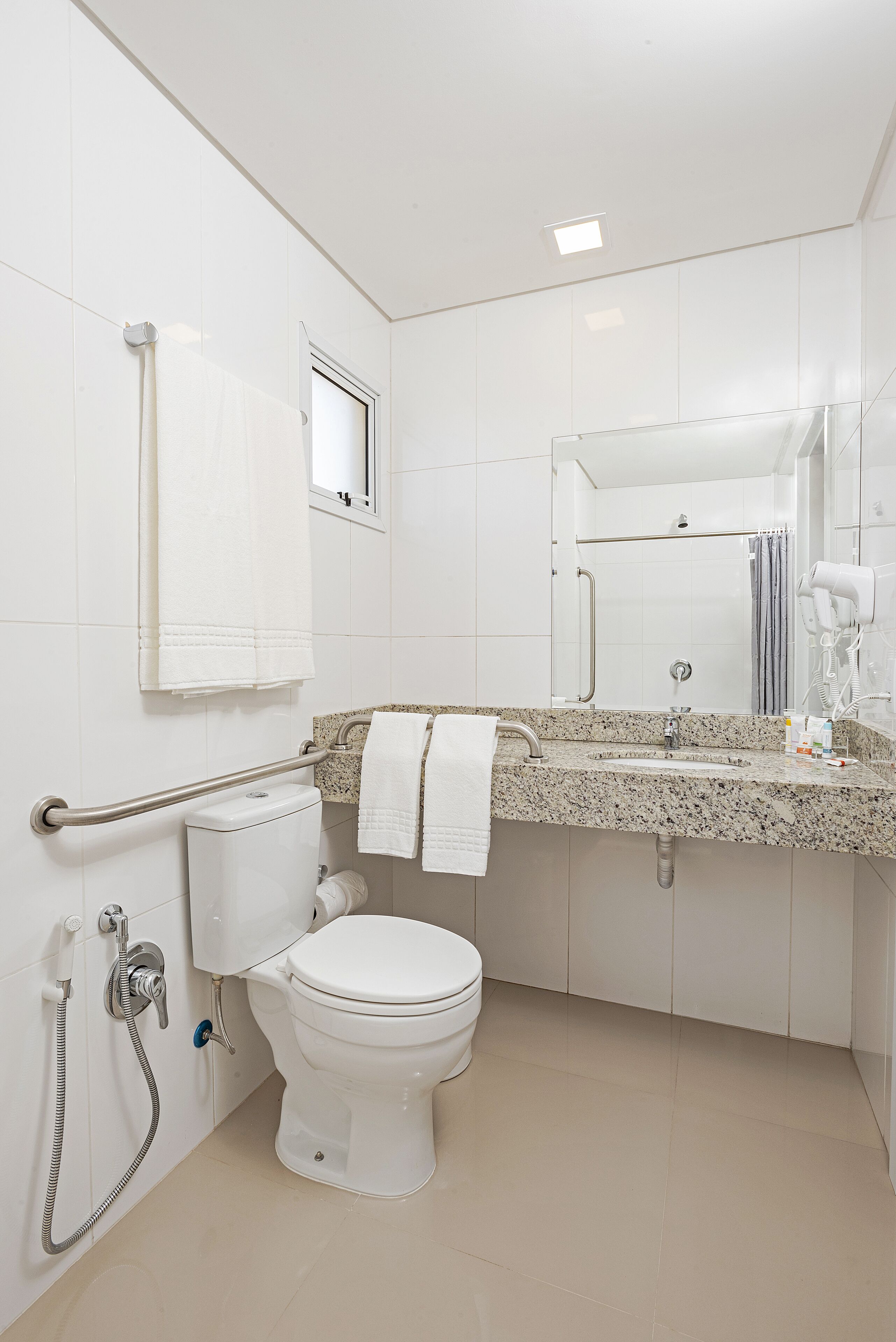Une salle de bain moderne avec des toilettes blanches, un lavabo doté d’un plan de travail en granit, un miroir et un sèche-mains.