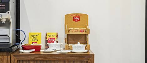 Habitación de hotel con escritorio de madera, cafetera, frutero y cartel que indica opciones sin gluten.
