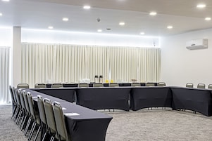 Un salón de conferencias con una larga mesa, sillas y un fondo de cortina blanca.