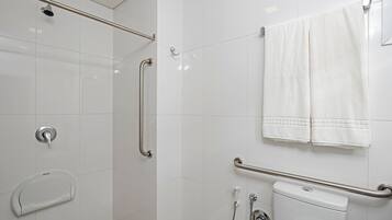 Un baño con azulejos blancos, inodoro, ducha con cabezal de ducha de mano y barras de apoyo.