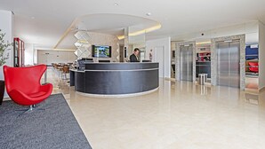 Eine moderne Hotelhalle mit einer Rezeption, einem roten Sessel und einem Fernseher.