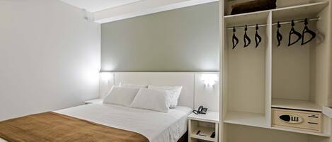 A modern hotel room with a neatly made bed, a bedside table with a phone, and a walk-in closet with hanging space.