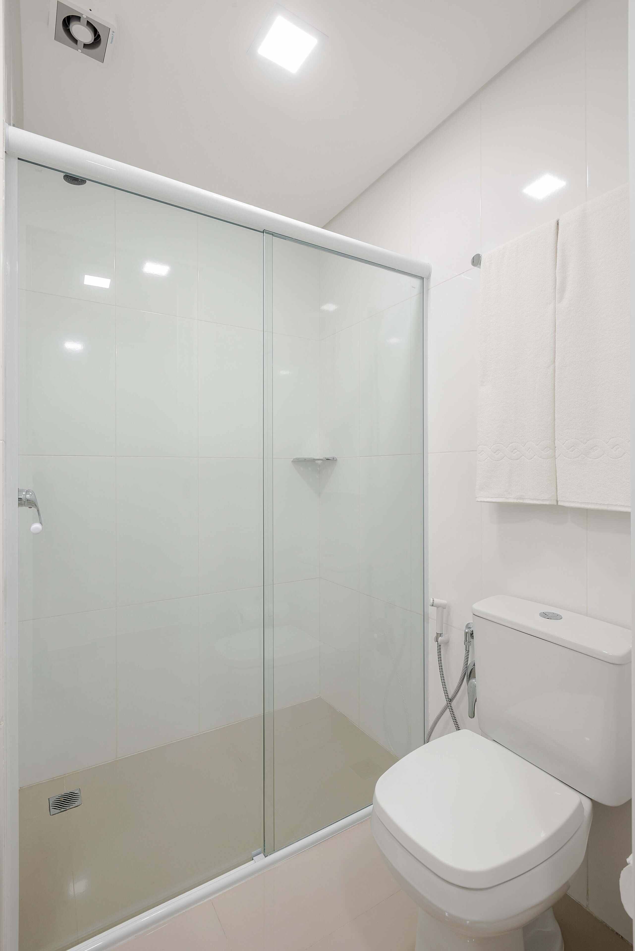 A modern bathroom with a glass-enclosed shower, a white toilet, and a towel hanging on the wall.