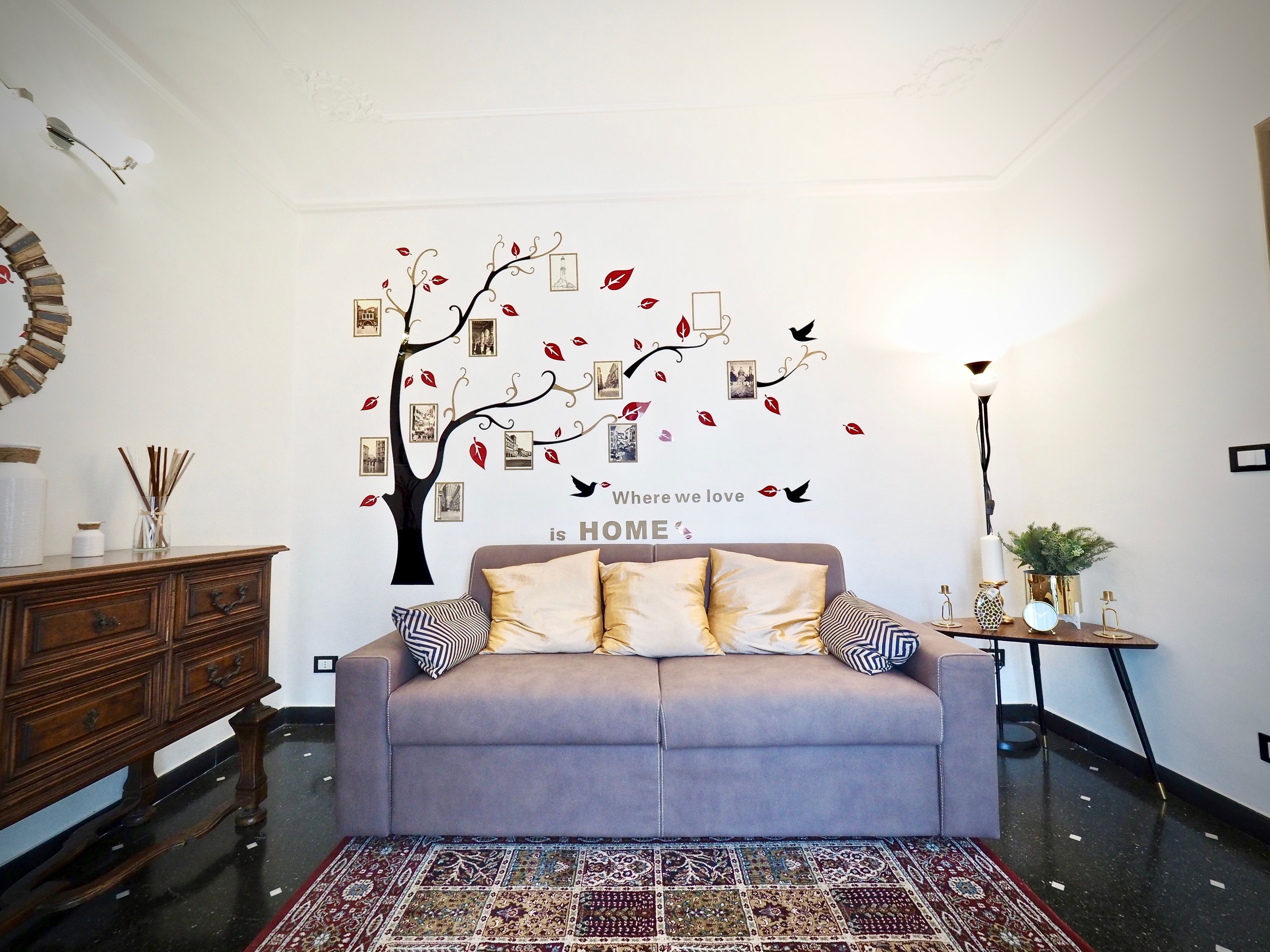 Un salon avec un canapé gris, un tapis à motifs et un mur décoré d’un arbre et de photos.