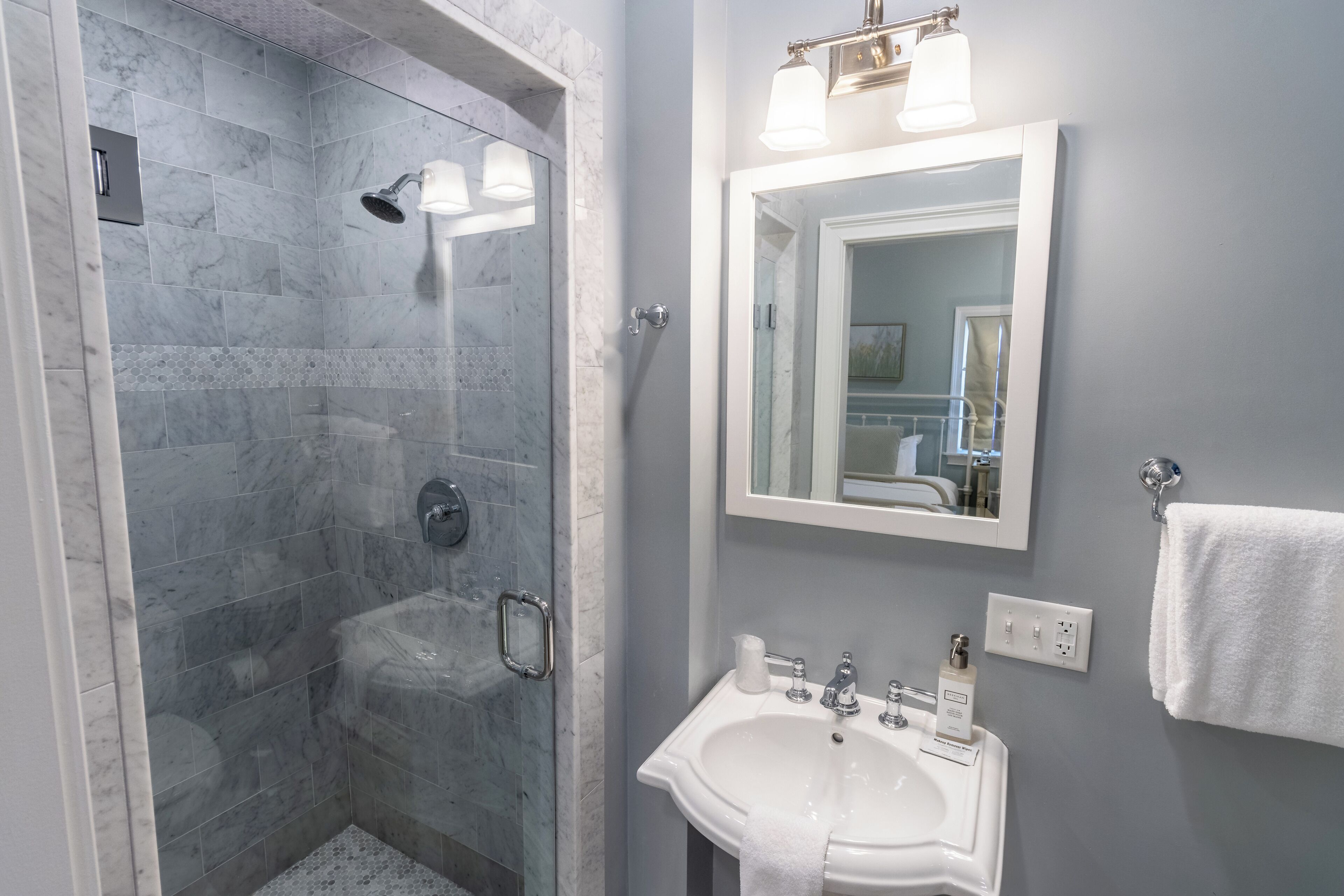 A bathroom with a glass-enclosed shower, a white sink, and a mirror above it.