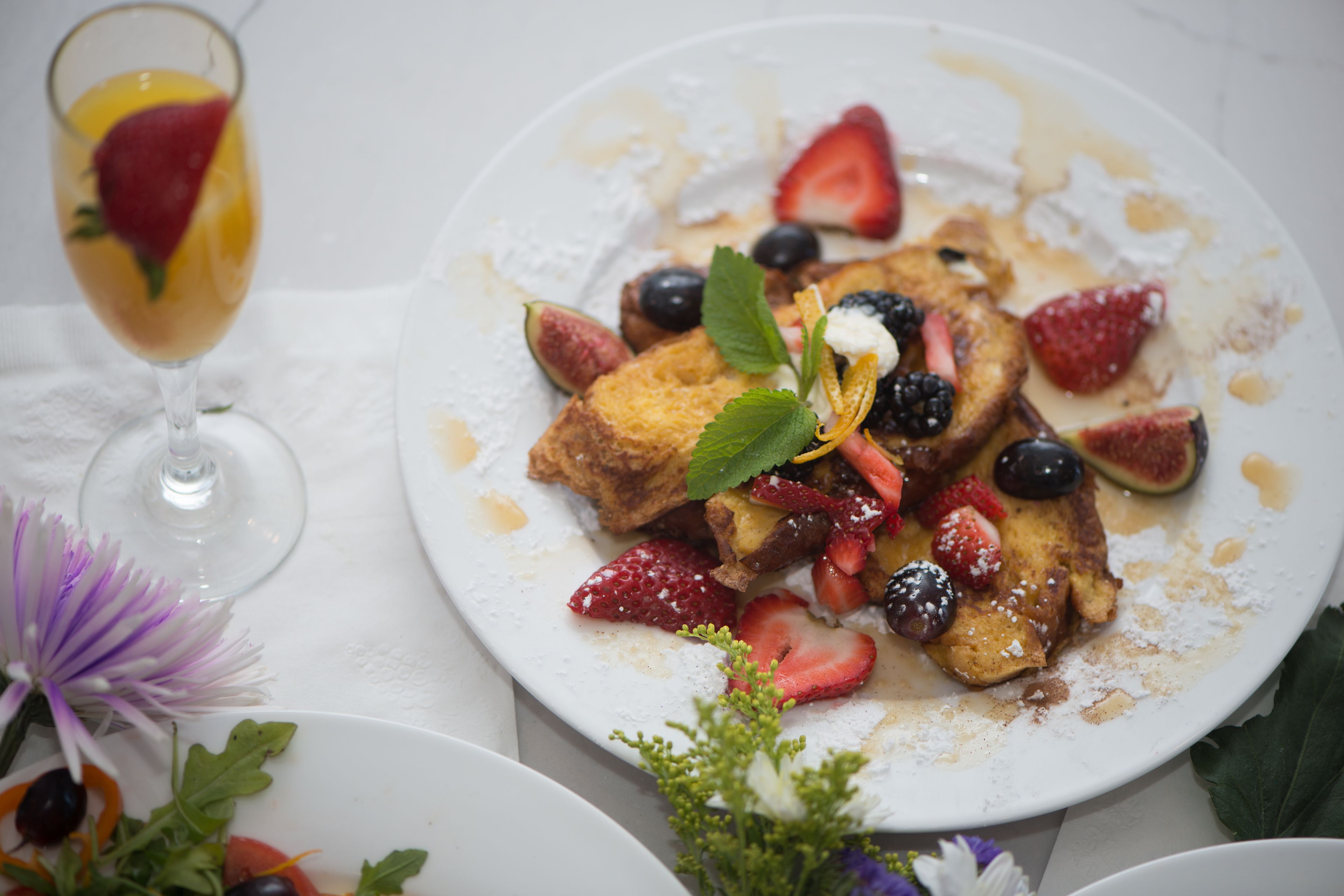 A breakfast plate with pancakes, strawberries, blueberries, and a glass of orange juice.