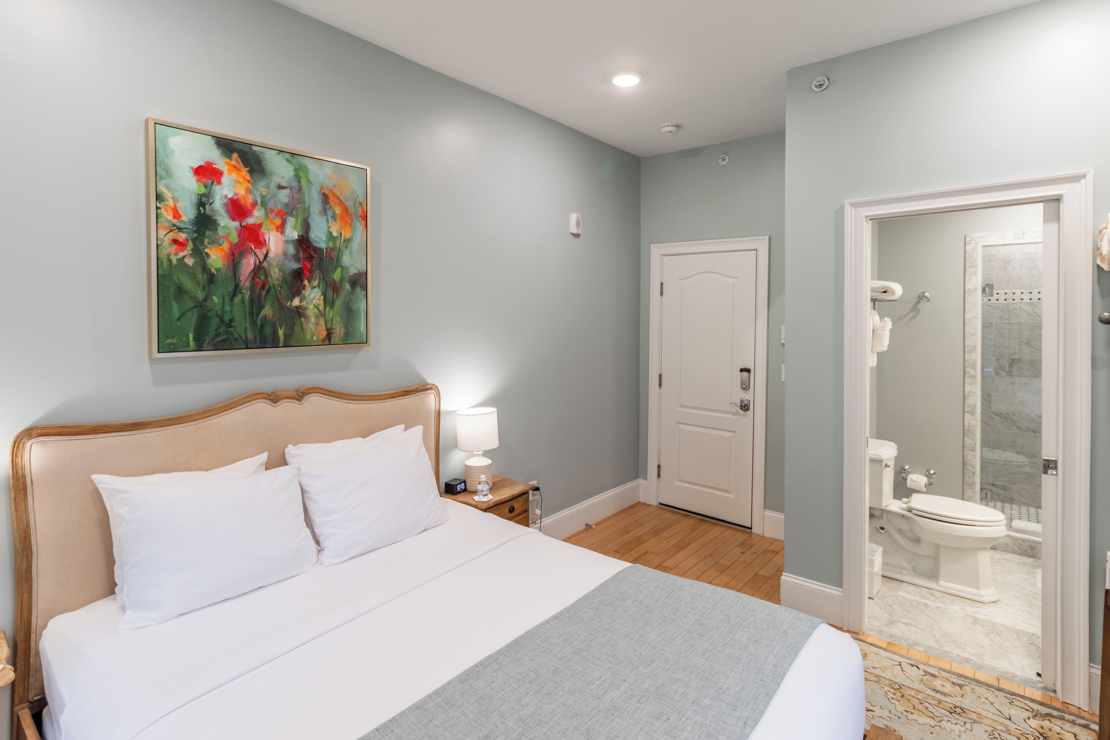 Quarto com cama, mesa de cabeceira, abajur e um quadro na parede.