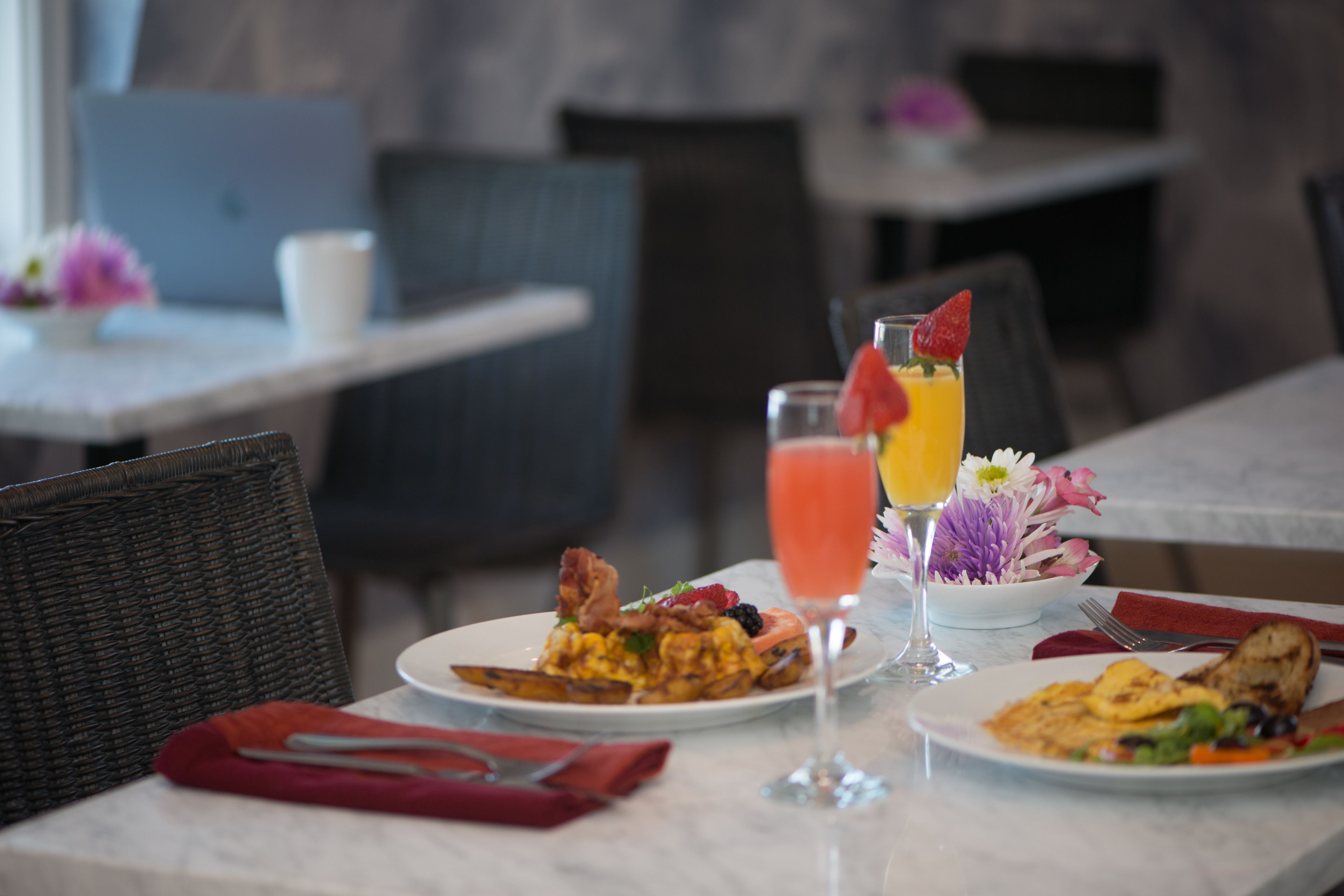 Une table à manger avec des assiettes remplies de nourriture, un verre de jus d’orange et un arrangement floral.