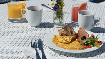 Una escena de desayuno con un plato de comida, dos tazas de café, un vaso de jugo de naranja y un vaso de bebida roja sobre una mesa blanca.