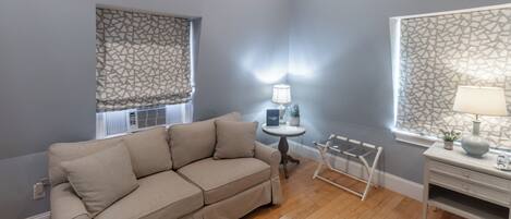 A modern living room with a beige sofa, a small round table with a lamp, and a decorative chair.