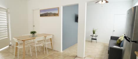 A modern kitchen with a dining area, a small table with chairs, a refrigerator, and a blue door.