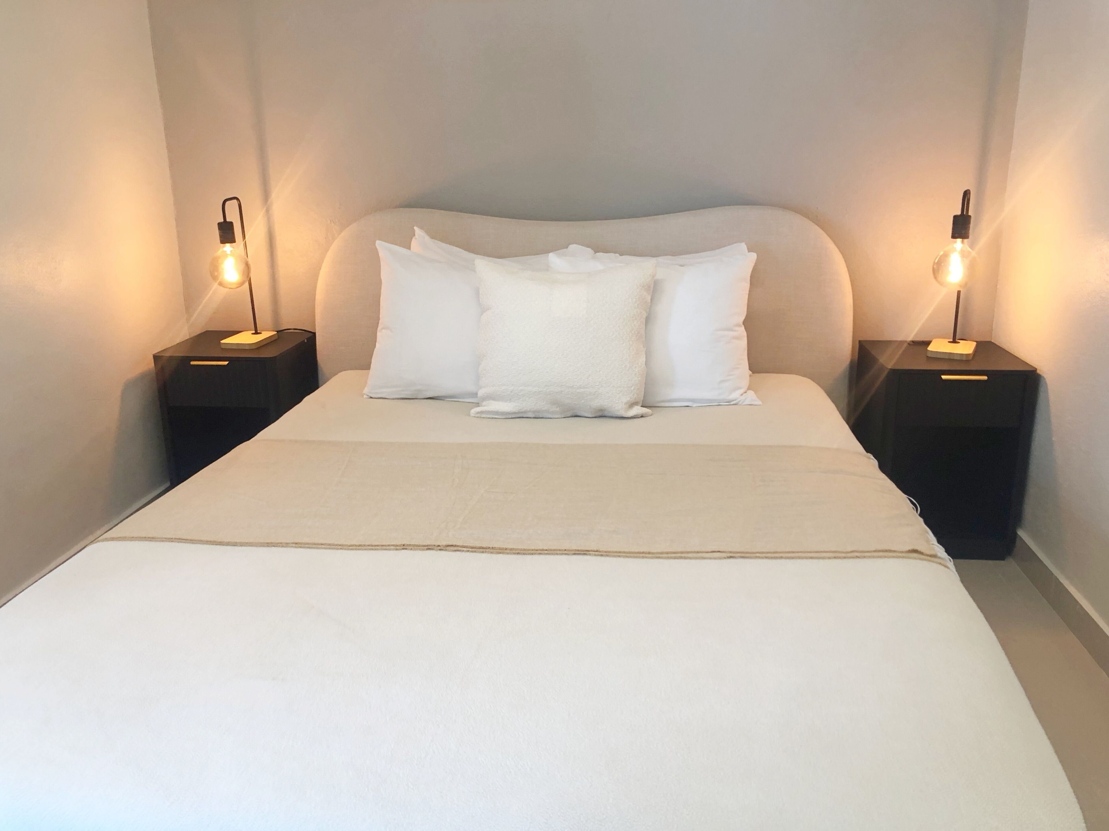 Un lit bien fait, avec du linge de lit et des oreillers blancs, flanqué de deux tables de chevet sur lesquelles sont posées des lampes.