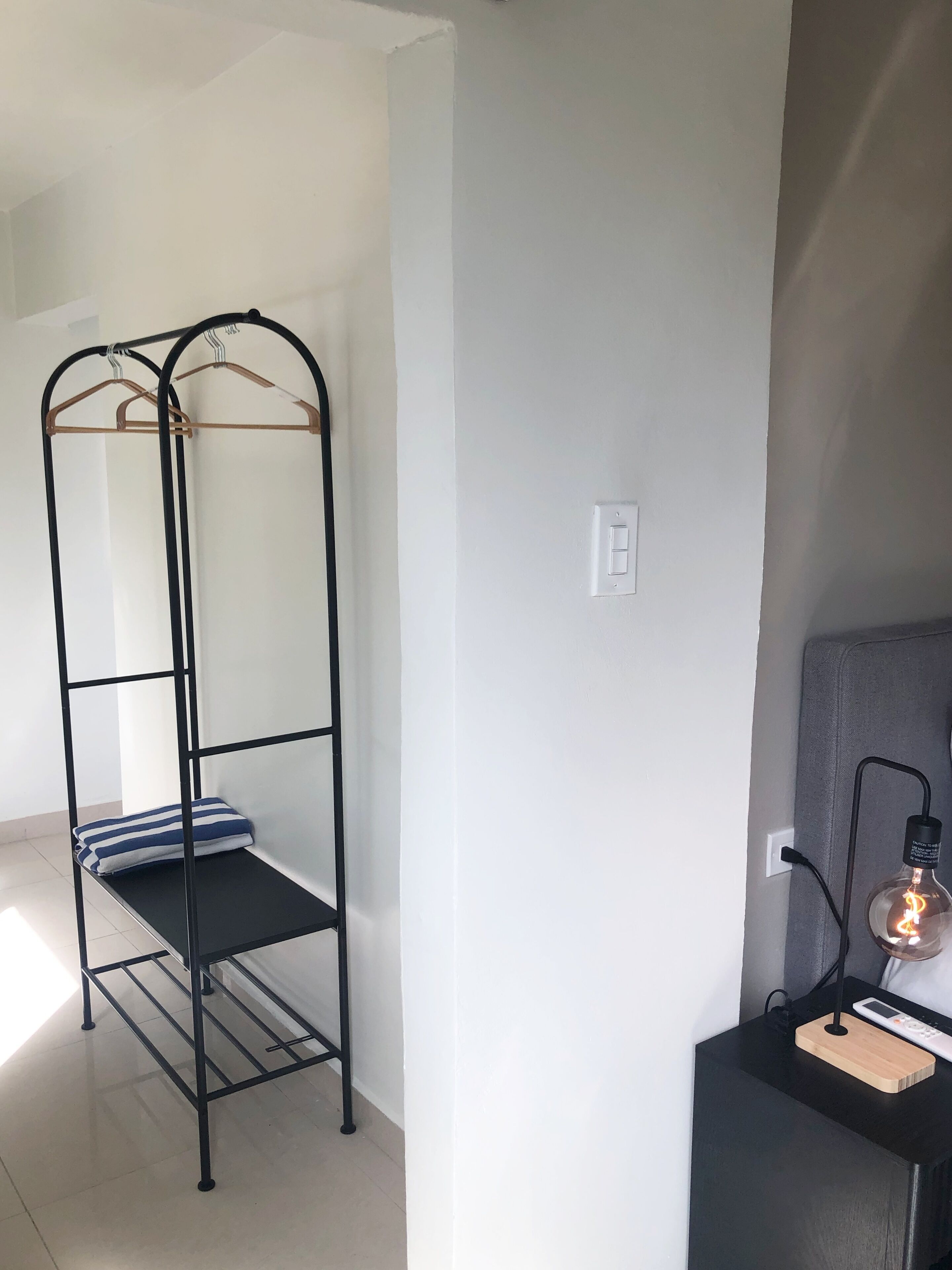 A bunk bed with a metal frame and wooden slats, a bedside table with a lamp, and a power outlet on the wall.