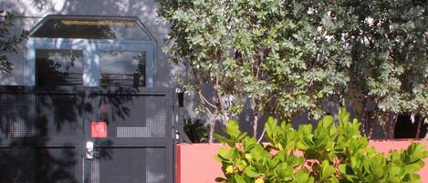 A building with a metal gate, a pink wall, and green foliage.