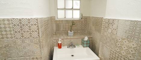 A bathroom with patterned tiles, a white sink, a window, and a shelf with toiletries.