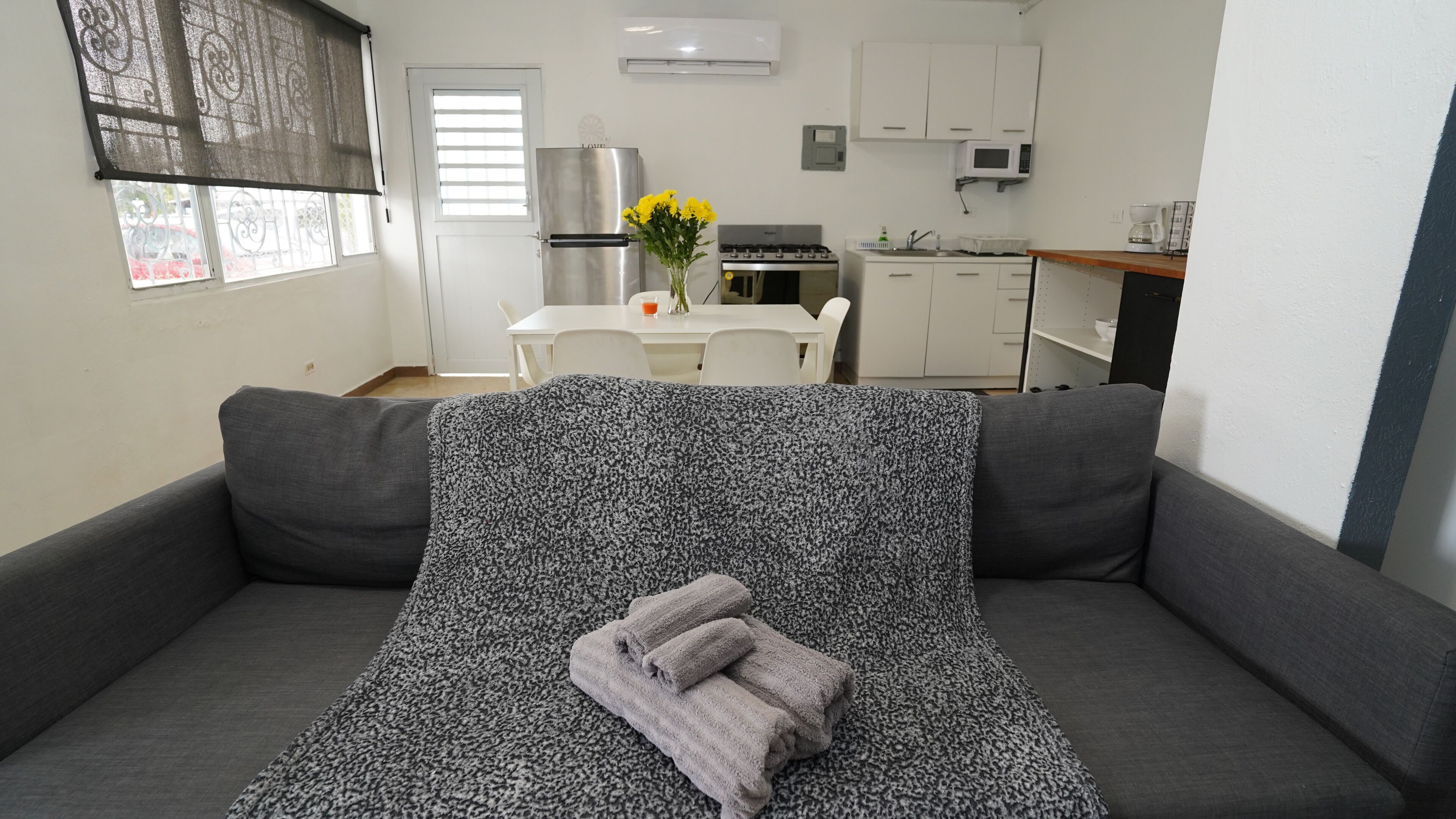 Een moderne woonkamer met een grijze bank, een decoratief plaid en een vaas met gele bloemen.