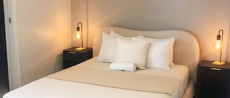 A modern bedroom with a large bed, two bedside tables with lamps, and an air conditioning unit on the wall.