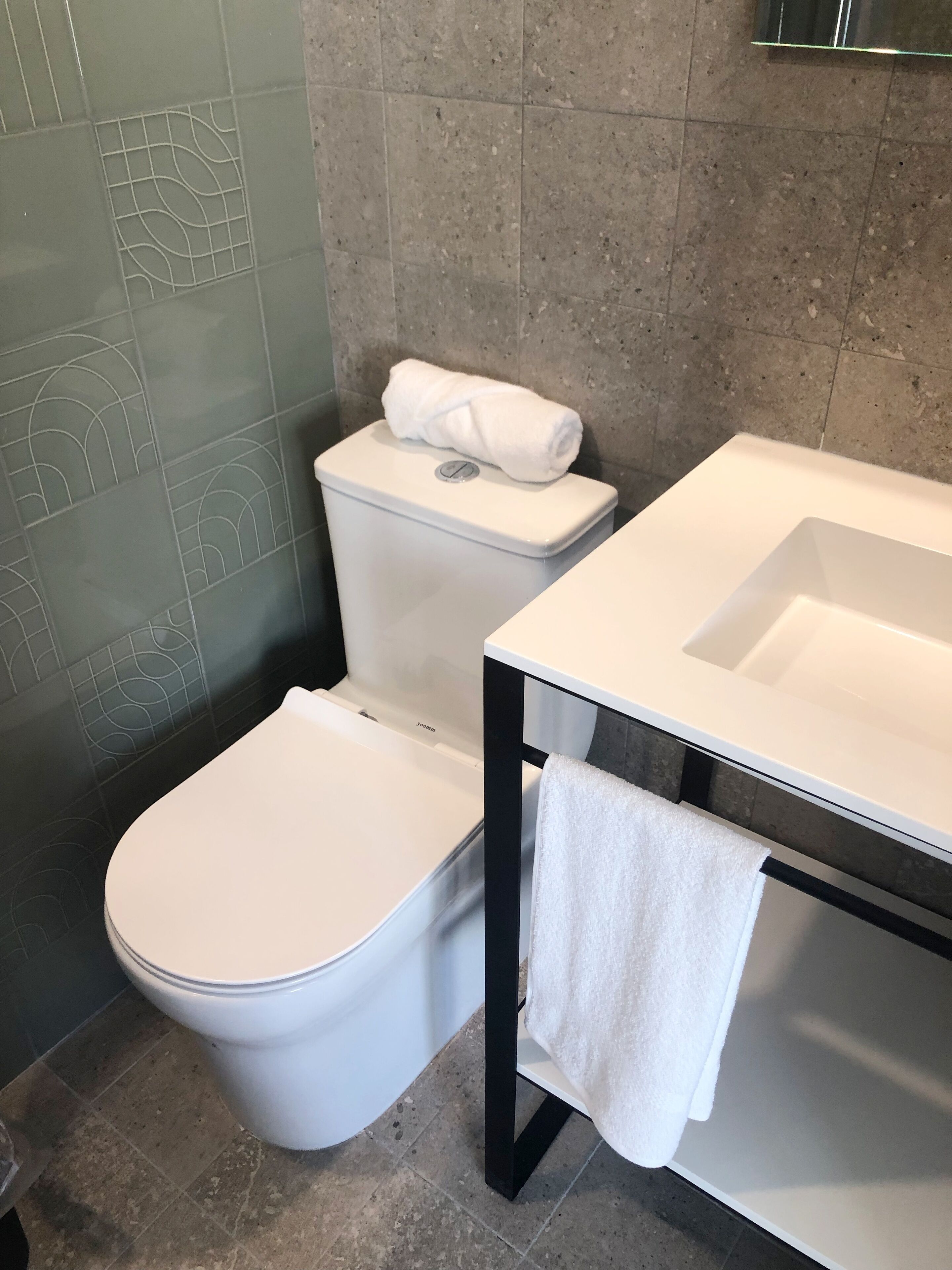 A modern bathroom with a white toilet, a white sink, and a towel hanging on the side.