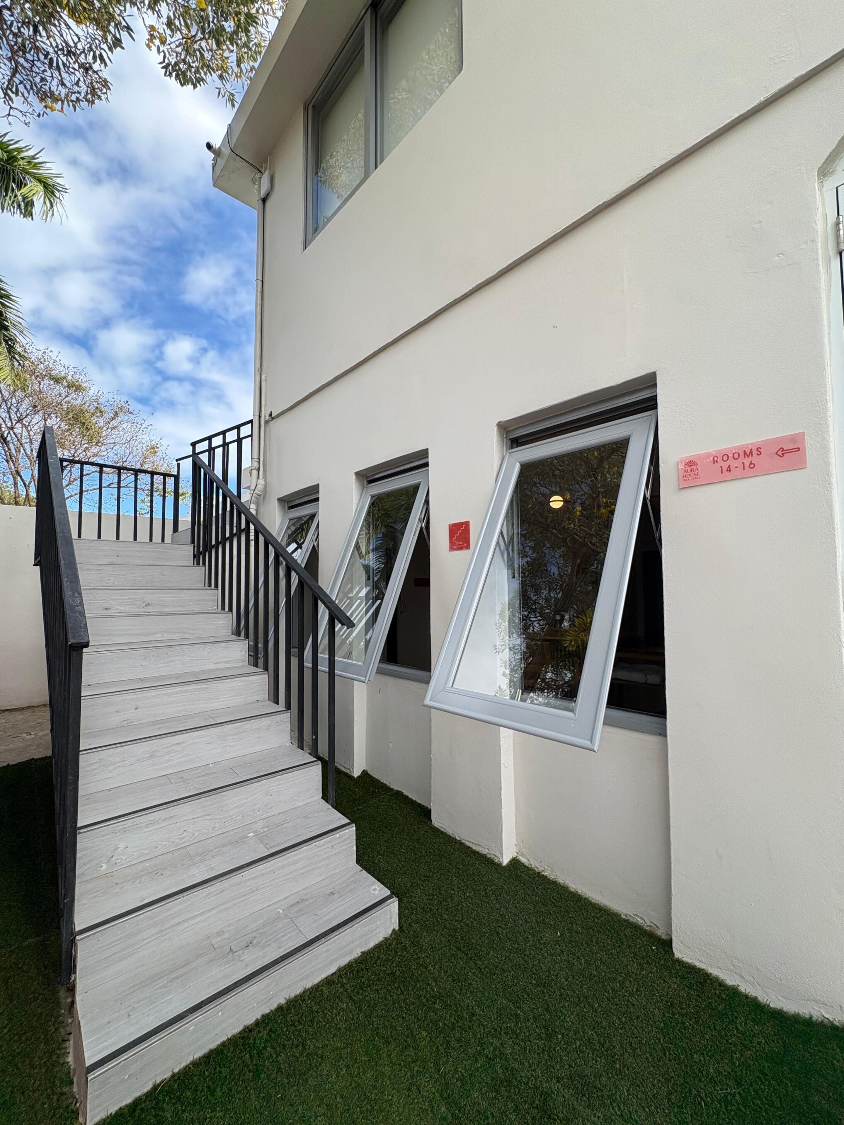 Um edifício com escadaria que leva a uma porta identificada com 'Quartos 14-16'.