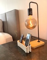A modern lamp with a glass shade and a remote control holder on a table.