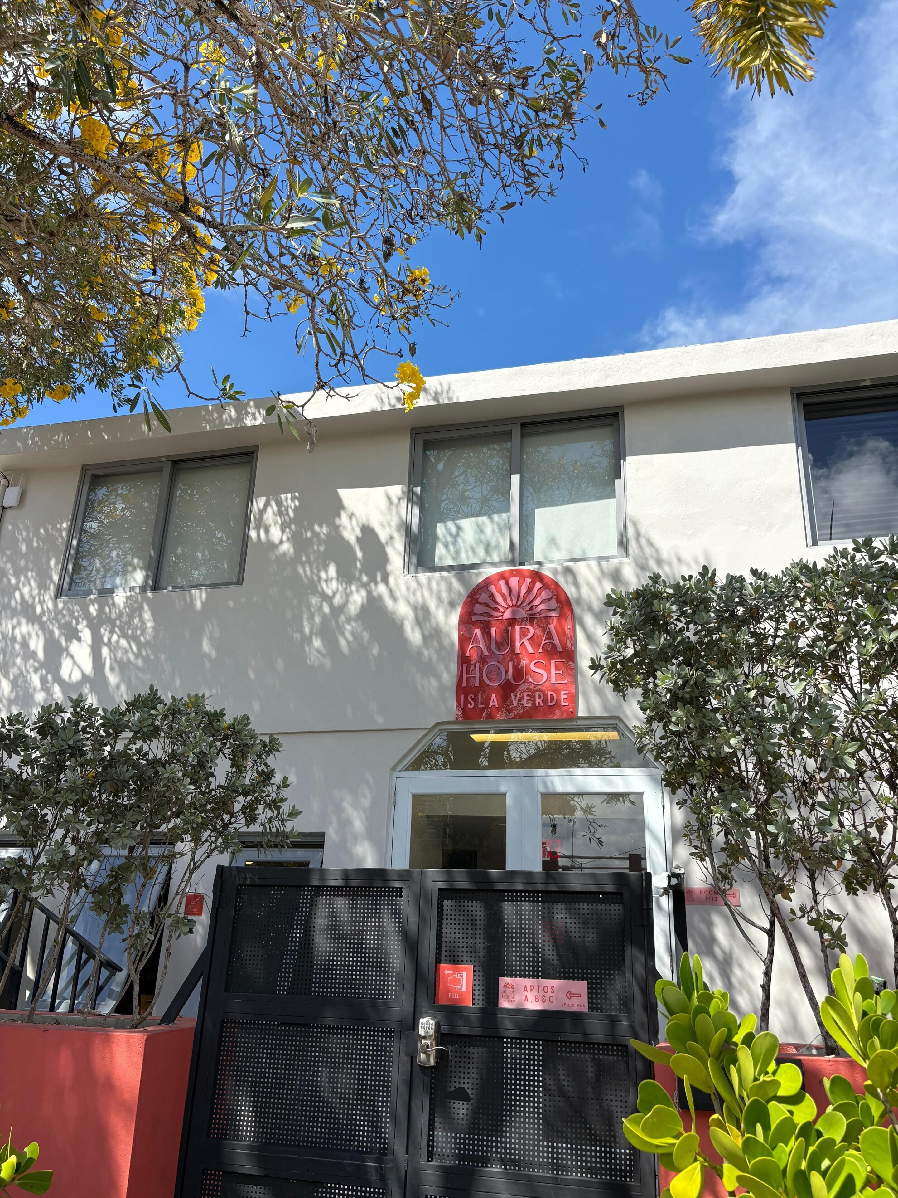 Ein Gebäude mit einem Schild, auf dem 'AURA HOUSE ISLA VERDE' steht, oberhalb eines einkreisenden Toress.